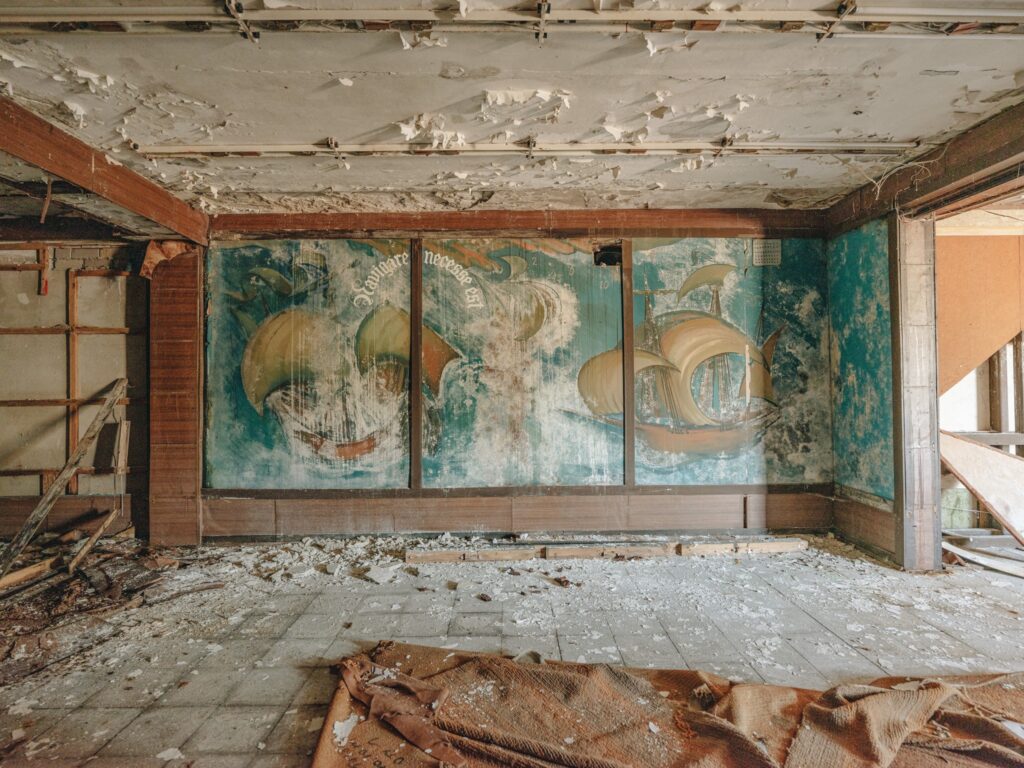 Open House Tallinn tuur Hundipeal. Fotol näha lagunenud seina, kus laest pudeneb krohvi ja põrand kaetud kiviklibuga. Seinal sinistes toonides maal, kus on kujutatud merd ja purjekaid.