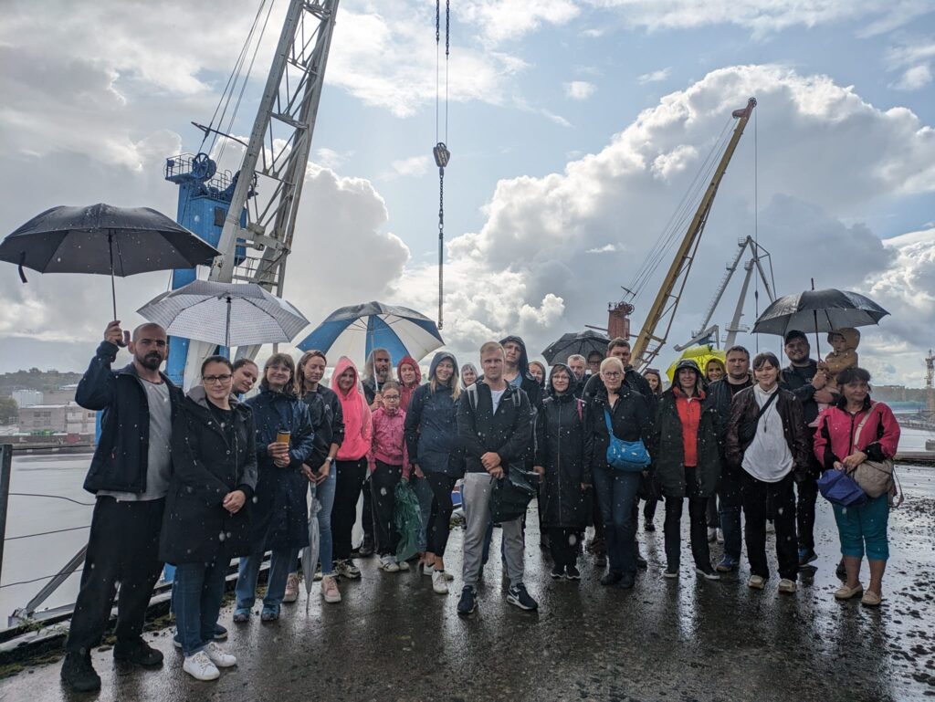 Koplikandi matkade erimatk Hundipeale. Fotol on tuuril osalenud seltskonna grupipilt ca 30 inimesega. Vihma sajab, ent grupp on rõõmus.